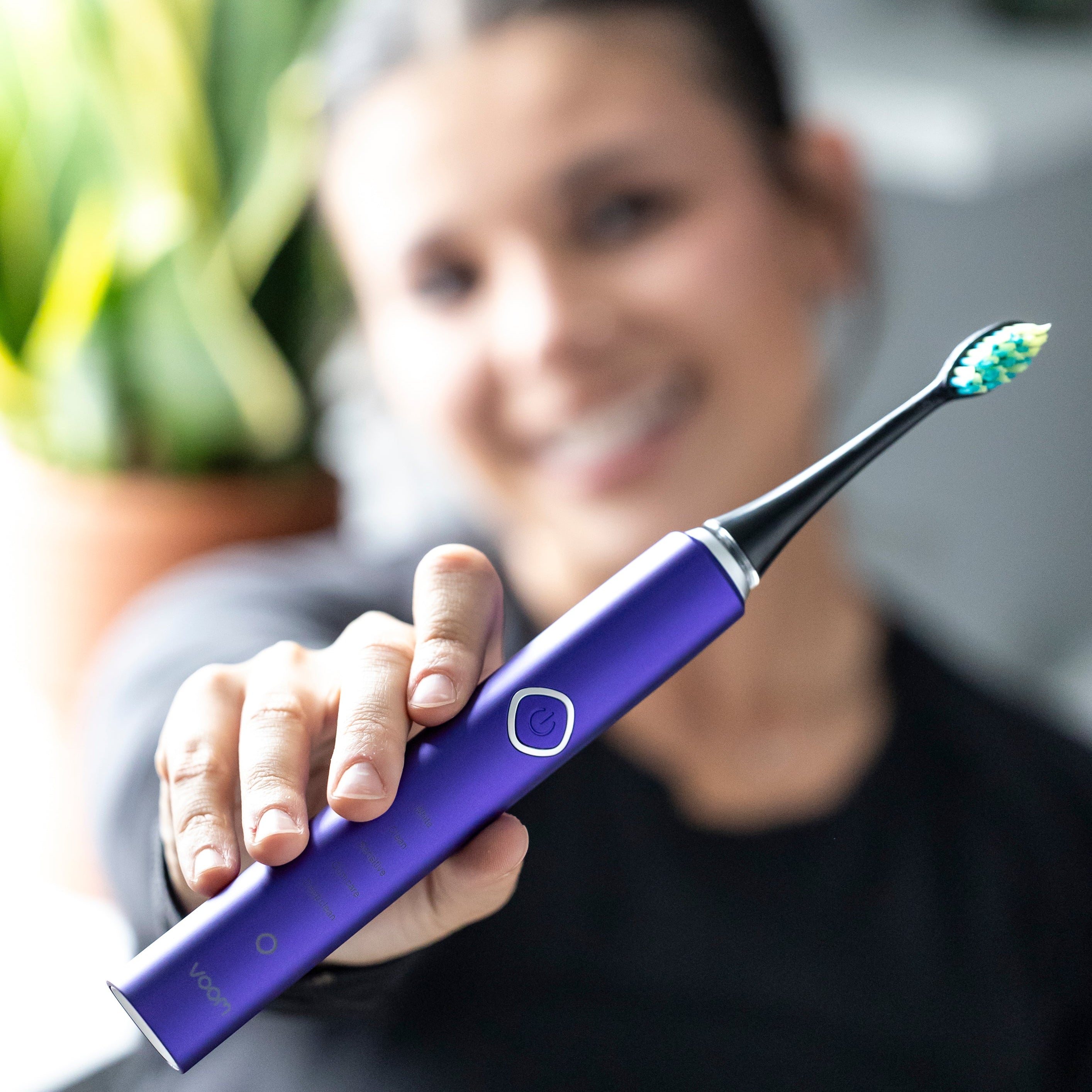 Person holding a purple electric toothbrush with a blurred background