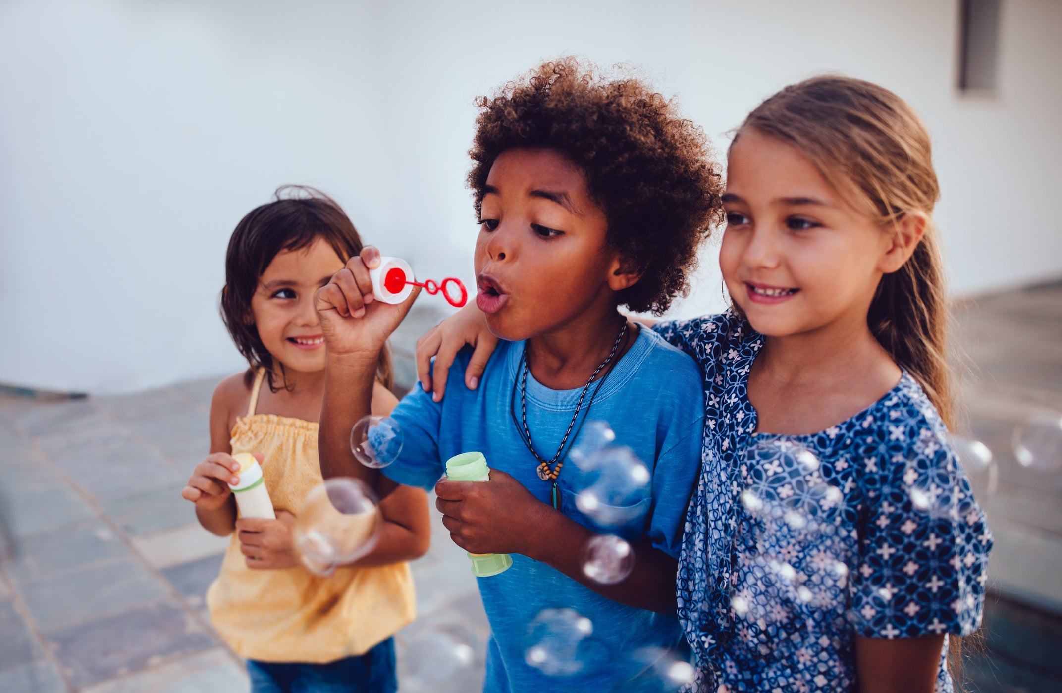 Three little girls smiling, blowing bubbles.