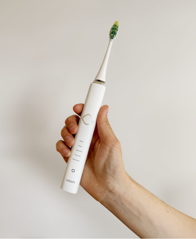 Hand holding a white electric toothbrush with a green bristle head against a plain background