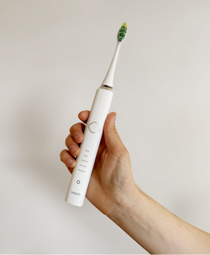 Hand holding a white electric toothbrush with a green bristle head against a plain background